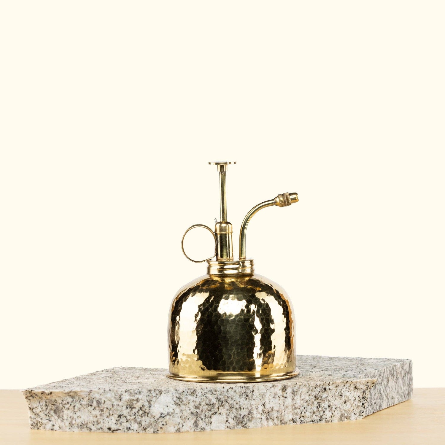 Gold metal spray mister on a stone surface with a white background